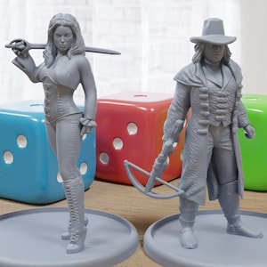 May include: Two grey painted figurines, one female with a sword and the other male with a crossbow, standing on grey bases. The figurines are surrounded by colourful dice.