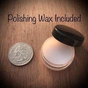 May include: A small, clear plastic jar with a black lid, containing white polishing wax. A U.S. quarter coin is next to the jar for size comparison. The text "Polishing Wax Included" is above the jar.