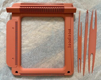 May include: An orange weaving loom with the word "loomloom" printed on the side. The loom is rectangular with a series of teeth along the top and bottom edges. Three weaving tools are next to the loom.
