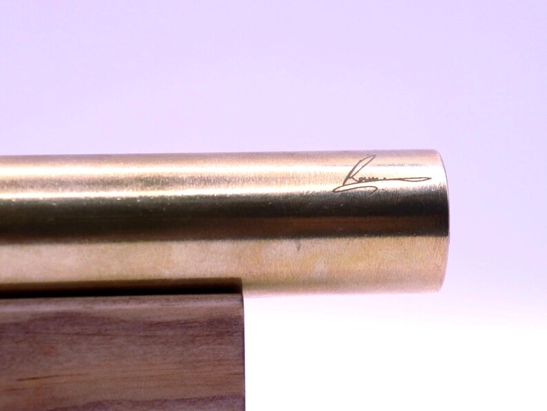 Close-up of the artist's signature or unique design detail etched onto the base of the handmade brass kaleidoscope. Confirms authenticity and collector value.