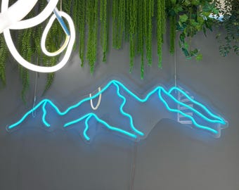 May include: A blue neon mountain range light fixture against a grey wall. The neon light is in the shape of a mountain range. Green hanging plants and a white light fixture are also visible.