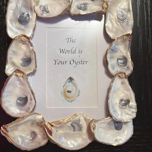 May include: A rectangular picture frame decorated with oyster shells. The shells are white with gold edges and surround a white background with the text "The World is Your Oyster". An oyster illustration is also present.