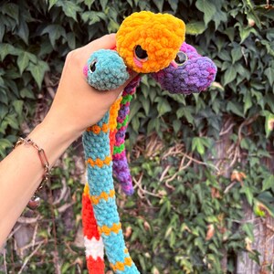 Peut inclure: Un jouet serpent en peluche &agrave; plusieurs t&ecirc;tes fabriqu&eacute; &agrave; partir de fil doux et duveteux dans des couleurs vives, notamment orange, turquoise, violet et rouge. Les trois t&ecirc;tes pr&eacute;sentent de grands yeux de s&eacute;curit&eacute; noirs brillants et des d&eacute;tails roses.