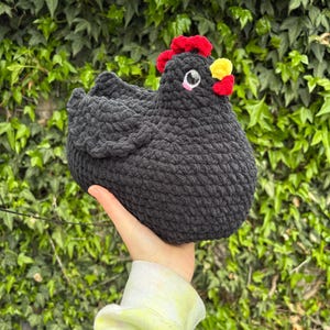 Peut inclure: Un jouet en peluche poulet crocheté à la main en fil gris anthracite foncé. La figurine présente une crête rouge vif, un bec jaune, une petite caroncule rouge et des yeux en plastique noir ronds avec un accent rose sous chaque œil.