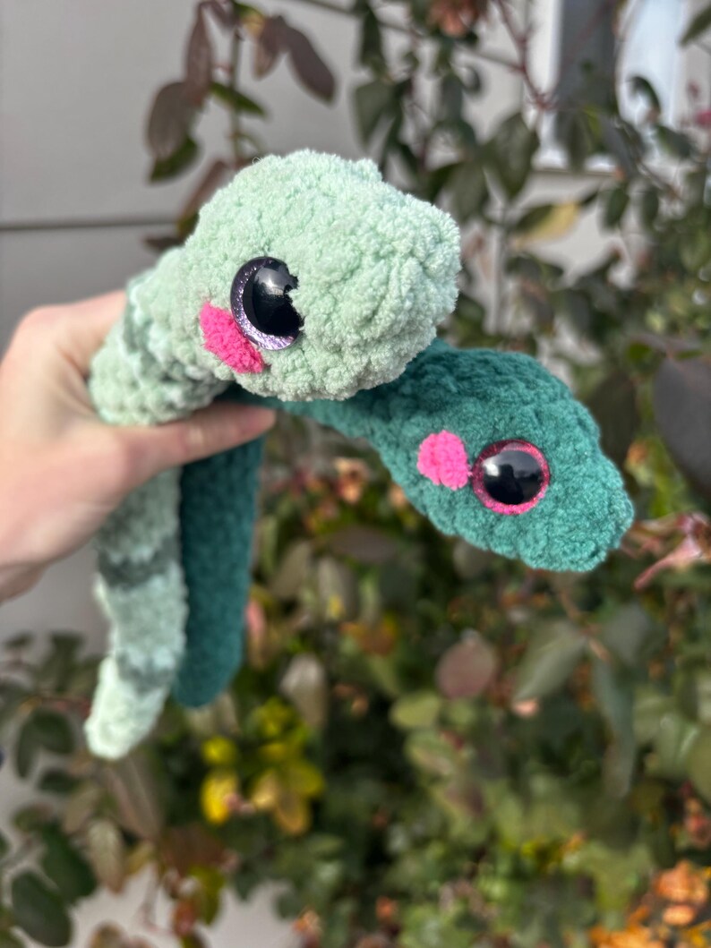 Peut inclure: Deux serpents en peluche fabriqu&eacute;s en fil doux et duveteux. L'un est vert menthe clair avec des rayures vert fonc&eacute;, et l'autre est d'un vert for&ecirc;t fonc&eacute; uni. Les deux serpents ont de grands yeux ronds en plastique noir et des joues roses.