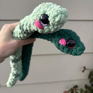 Peut inclure: Deux serpents en peluche fabriqu&eacute;s en fil textur&eacute; doux. L'un est vert menthe clair et l'autre est vert for&ecirc;t fonc&eacute;. Ils poss&egrave;dent tous deux de grands yeux ronds en plastique noir avec des reflets violets et de petites joues en laine rose vif.