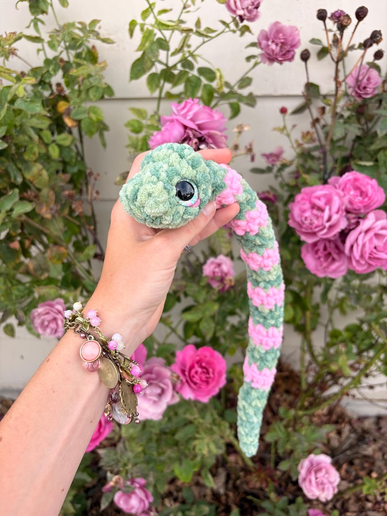 Peut inclure: Un serpent en crochet compos&eacute; d'un fil textur&eacute; doux avec des segments altern&eacute;s de vert sauge et de rose bonbon. Le serpent poss&egrave;de une t&ecirc;te arrondie avec un grand &oelig;il de s&eacute;curit&eacute; noir brillant dot&eacute; d'un iris bleu clair et d'un reflet blanc.