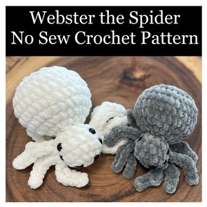 May include: Two crocheted spiders, one white and one gray, with black eyes. The spiders are sitting on a wooden surface. The text "Webster the Spider No Sew Crochet Pattern" is displayed above the spiders.