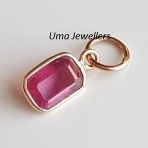 May include: A gold pendant featuring a rectangular, faceted pink gemstone set in a smooth bezel, with a circular jump ring attached at the top. The text Uma Jewellers is printed above the pendant, which has a polished metallic finish.