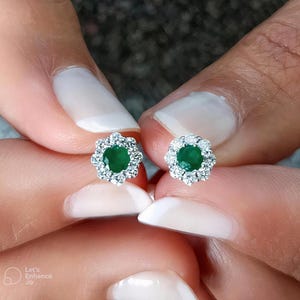 Può includere: Un paio di orecchini a lobo in argento con una pietra preziosa verde circondata da un'aureola di piccole pietre bianche.