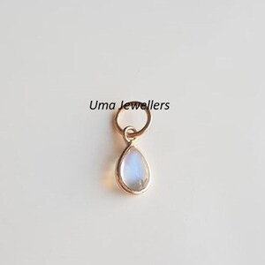 May include: A gold charm with a teardrop-shaped moonstone pendant. The charm has a small loop at the top for attaching to a necklace or bracelet.