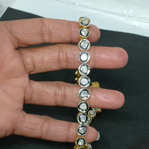 May include: A gold chain necklace with a row of round, bezel-set diamonds. The diamonds are all different sizes and shapes, and they are set in a black metal frame.