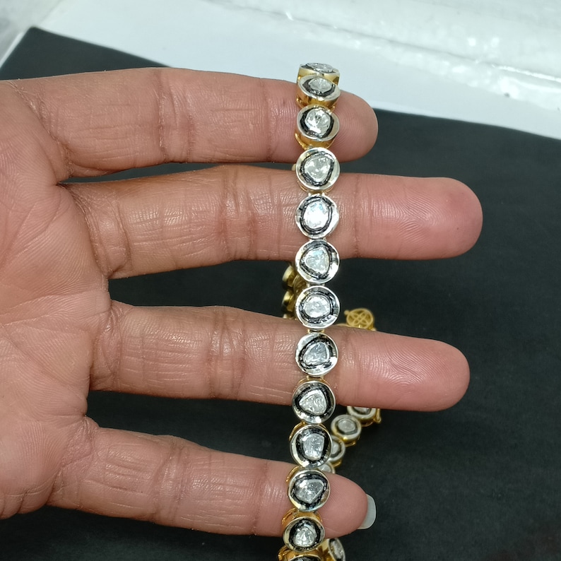 May include: A gold chain necklace with a row of round, bezel-set diamonds. The diamonds are all different sizes and shapes, and they are set in a black metal frame.