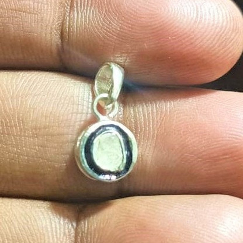 May include: A silver pendant with a round, white stone set in a black bezel. The pendant is on a silver chain.