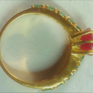 May include: A gold ring featuring a red and green stone setting. The ring is adorned with a row of green stones around the band.