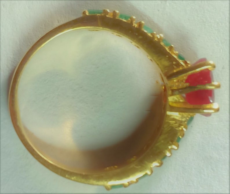 May include: A gold ring featuring a red and green stone setting. The ring is adorned with a row of green stones around the band.