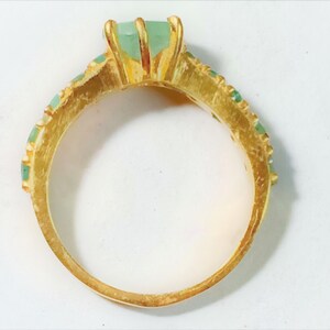 May include: A gold ring with a large green gemstone and smaller green gemstones around the band.