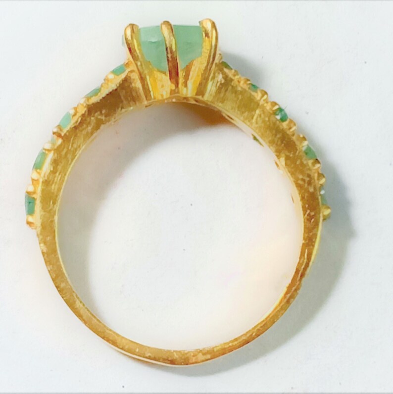 May include: A gold ring with a large green gemstone and smaller green gemstones around the band.