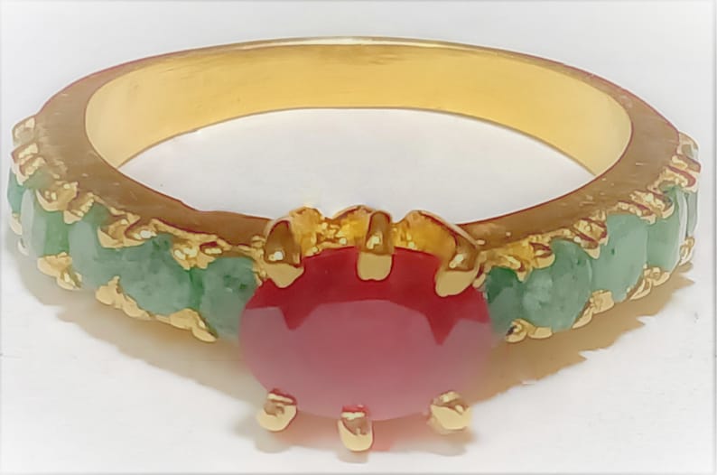 May include: A gold ring featuring a large red gemstone surrounded by smaller green gemstones.