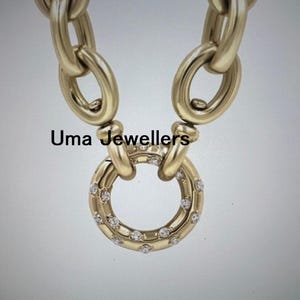 Peut inclure: Collier doré avec de grands maillons ovales et un pendentif circulaire. Le pendentif est orné de petits diamants scintillants. Le texte "Uma Jewellers" est visible.