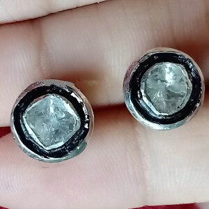 May include: A pair of silver earrings with a black border and a clear, faceted gemstone in the center.