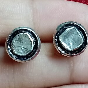 May include: A pair of silver earrings with a round, clear stone set in a black bezel. The stones have a rough, faceted texture.