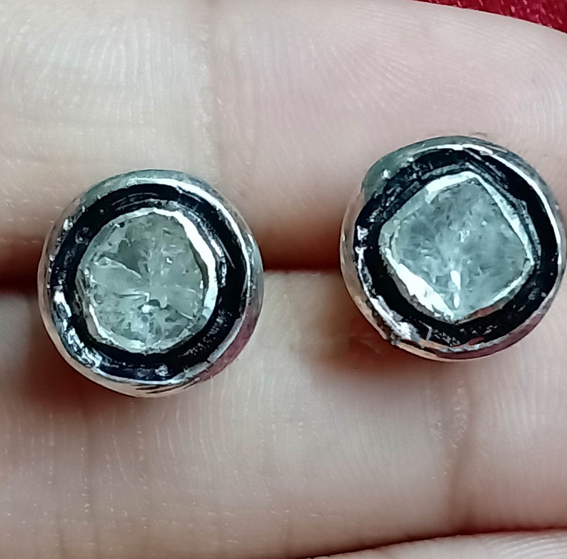 May include: A pair of silver earrings with a round, clear stone set in a black bezel. The stones have a rough, faceted texture.