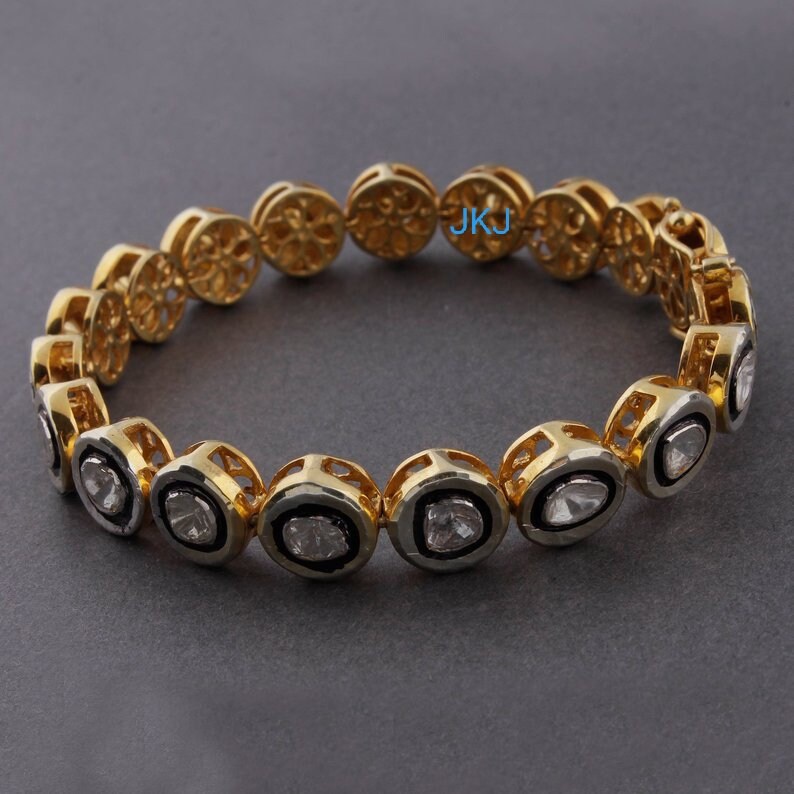 May include: A gold bracelet with a delicate filigree design and oval-shaped clear stones set in a silver bezel. The bracelet has a clasp closure.