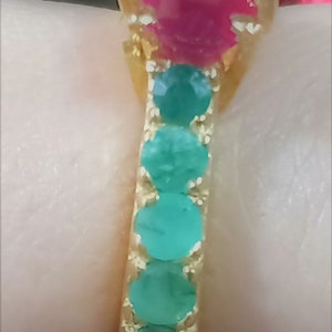 May include: A gold ring featuring a large pink gemstone surrounded by smaller green gemstones.