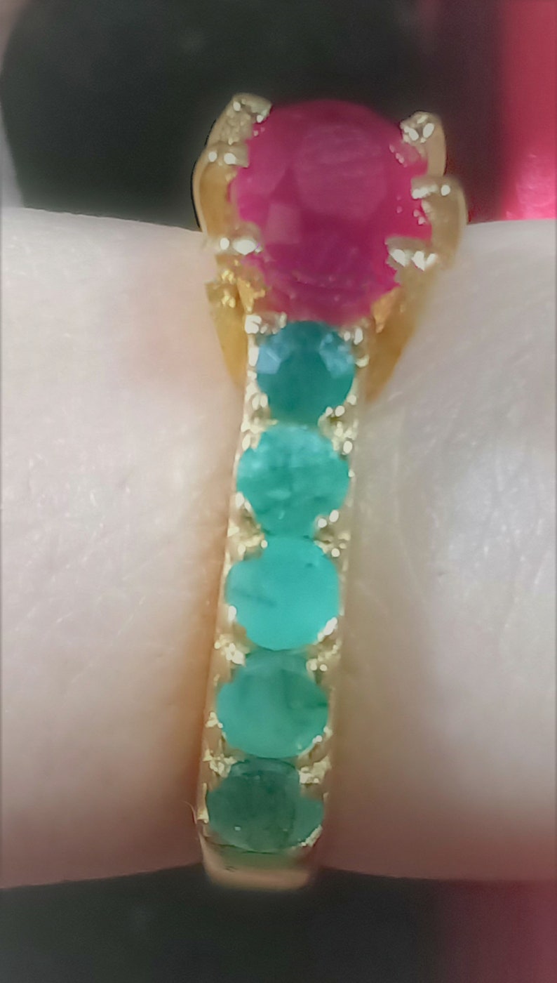 May include: A gold ring featuring a large pink gemstone surrounded by smaller green gemstones.