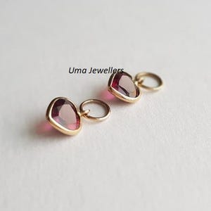 May include: Two gold heart-shaped charms with red gemstones. The charms have a small loop for attaching to a necklace or bracelet.