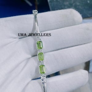 Peut inclure: Un bracelet en argent avec quatre pierres précieuses vertes. Le bracelet est sur une surface blanche. UMA JEWELLERS est écrit sur la surface.