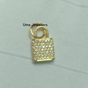 Puede incluir: Un colgante de candado dorado incrustado con numerosas piedras preciosas blancas pequeñas y brillantes. El colgante tiene una parte superior curva y un cuerpo rectangular. El texto "Uma Jewellers" es visible.