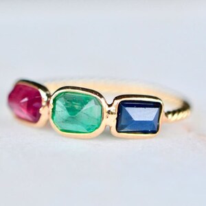 May include: A gold ring with three gemstones: a red ruby, a green emerald, and a blue sapphire.
