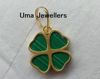 May include: A gold-colored pendant in the shape of a four-leaf clover. The clover's leaves are filled with green malachite. The text "Uma Jewellers" is printed in black on the top left of the image. The pendant is on a white surface.