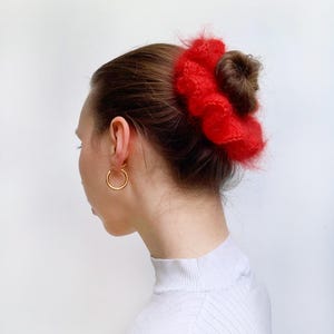 Puede incluir: Un coletero rojo y peludo usado en el cabello de una mujer, recogido en un mo&ntilde;o.