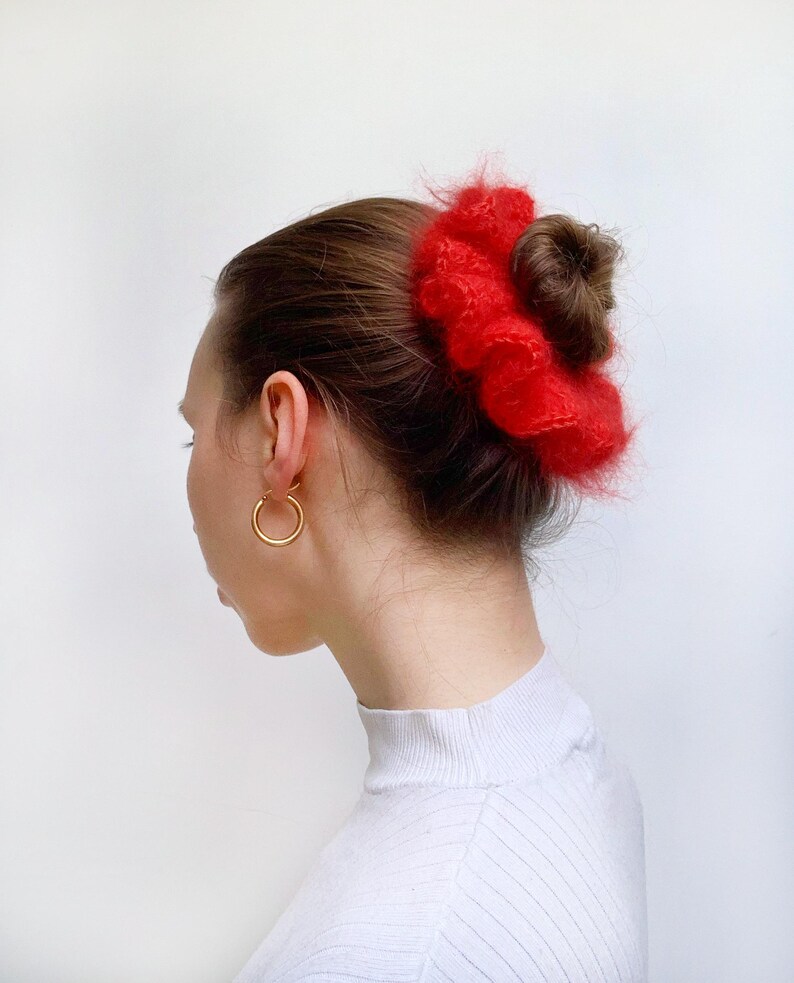 Puede incluir: Un coletero rojo y peludo usado en el cabello de una mujer, recogido en un mo&ntilde;o.