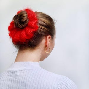 Puede incluir: Un coletero rojo y peludo con una textura arrugada. El coletero se lleva en el pelo de una mujer.