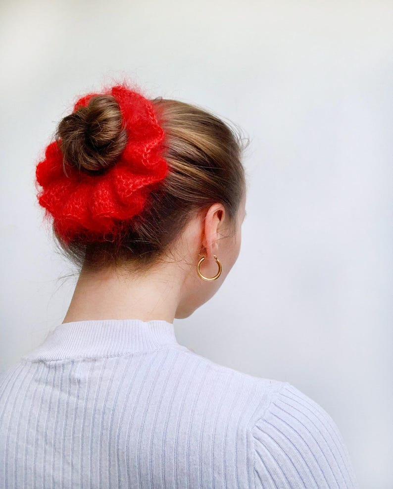 Puede incluir: Un coletero rojo y peludo con una textura arrugada. El coletero se lleva en el pelo de una mujer.