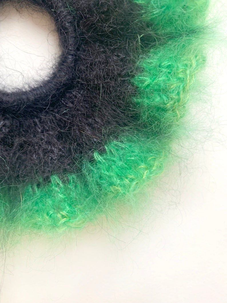 May include: A close-up of a handmade scrunchie with a fluffy texture. The scrunchie features alternating bands of black and bright green yarn. The scrunchie is set against a white background.