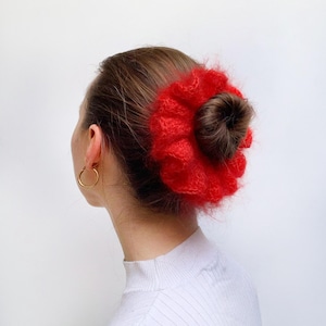 Puede incluir: Un coletero rojo y peludo con forma de flor. El coletero se lleva en el pelo de una mujer.