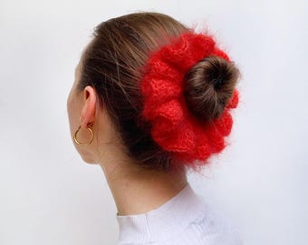 May include: A red fuzzy hair scrunchie in the shape of a flower. The scrunchie is worn in a woman's hair.