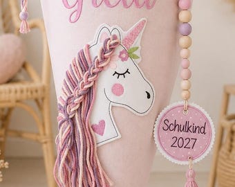 Puede incluir: Una bolsa de regalo cónica de color rosa claro con el nombre Greta bordado en letra cursiva rosa. Está rematada con tul rosa y decorada con una aplicación de unicornio con crines de hilo y una etiqueta redonda que dice Schulkind 2027.
