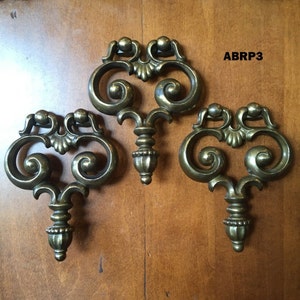 Può includere: Tre pomelli per armadi in metallo dorato decorati con un design a forma di cuore e intricati motivi a spirale. I pomelli hanno un pomo decorativo nella parte inferiore.