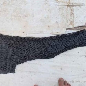 May include: Two pieces of black chainmail armor, likely for the arms or shoulders. The chainmail is made of small metal rings linked together.