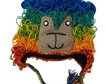 Puede incluir: Un colorido gorro de punto con la cara de una llama y una melena de colores del arcoíris. El gorro tiene una cara marrón con ojos blancos y una boca cosida en negro. La melena pasa del rojo al naranja, amarillo, verde y azul.