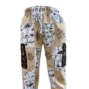 May include: Beige patchwork pants with a mushroom and flower design. The pants have a drawstring waist and side pockets.