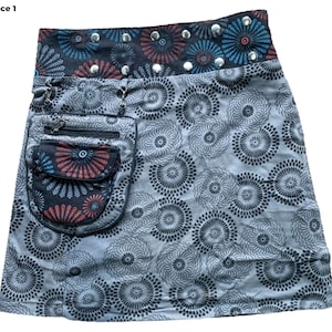 May include: A gray skirt with a black and white circular pattern. The skirt has a black waistband with a red, blue, and black patterned band and silver studs. The skirt has a large black pocket with a zipper and a smaller red, blue, and black patterned pocket.