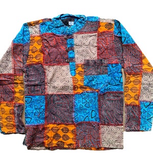 May include: A long-sleeved patchwork shirt featuring a mix of colours and patterns, including orange, blue, red, and brown. The shirt has a button-up collar and a pocket on the left side.