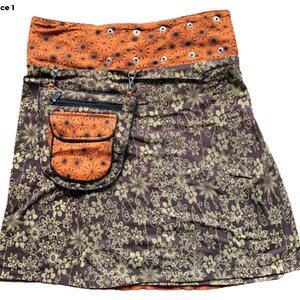 May include: A brown and orange skirt with a floral print. The skirt has a large pocket on the front with a zipper closure. The waistband is orange and has a row of silver eyelets.